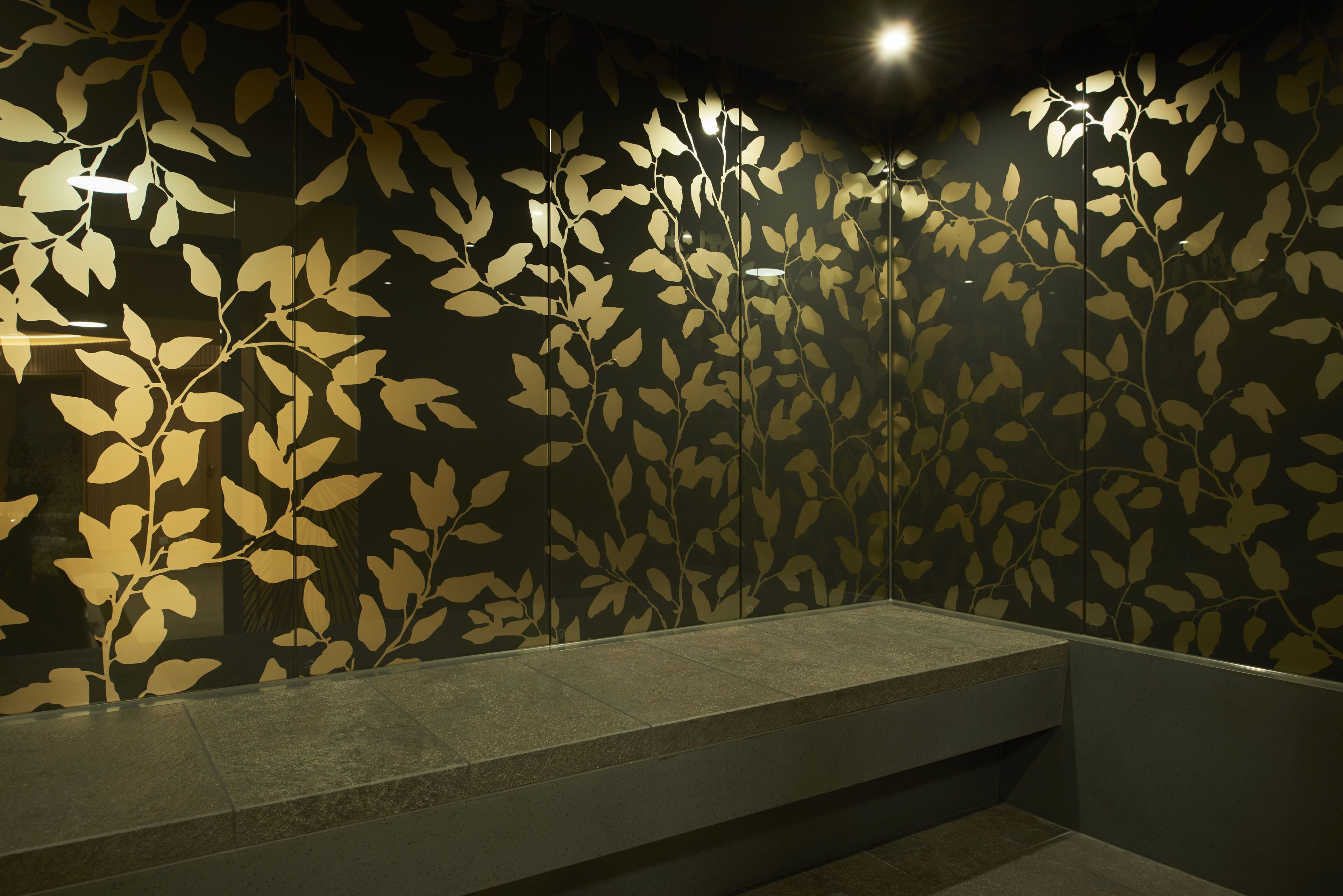 A modern bathroom with a large mirror, a bench, and a wall with a leaf pattern.