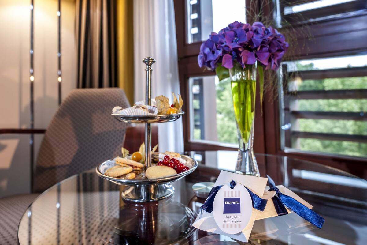 A three-tiered dessert stand with various sweets, a vase with purple flowers, and a tag with the text 'Dortm'.