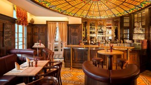 Una zona de bar con mobiliario de madera, techo de vitral y barra con botellas y vasos.