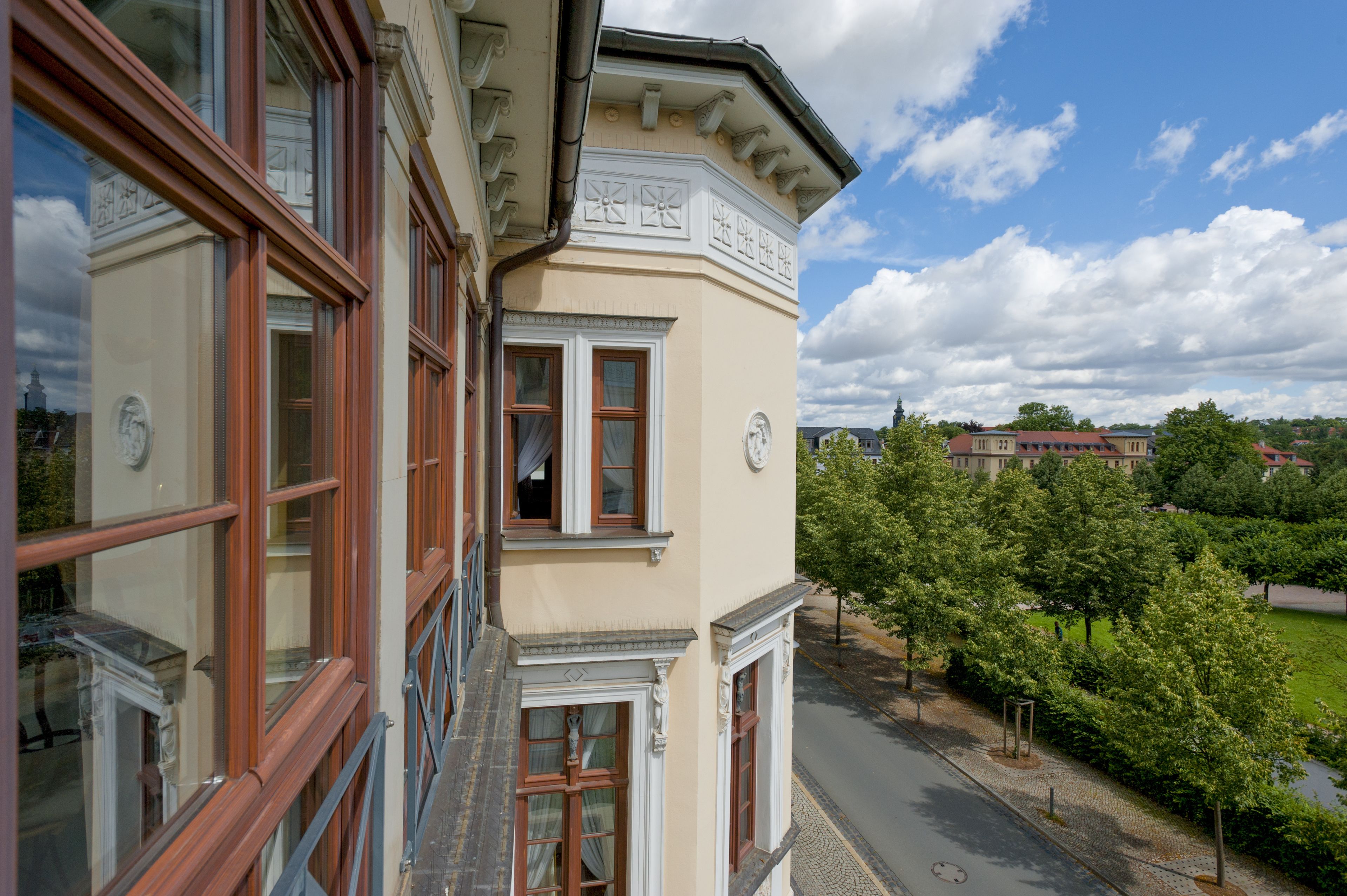 A corner building with a balcony, large windows, and a view of a park and distant buildings.