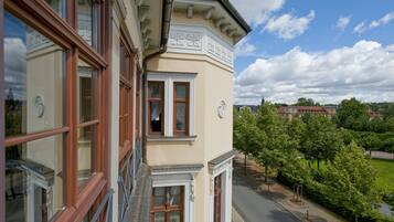 A corner building with a balcony, large windows, and a view of a park and distant buildings.