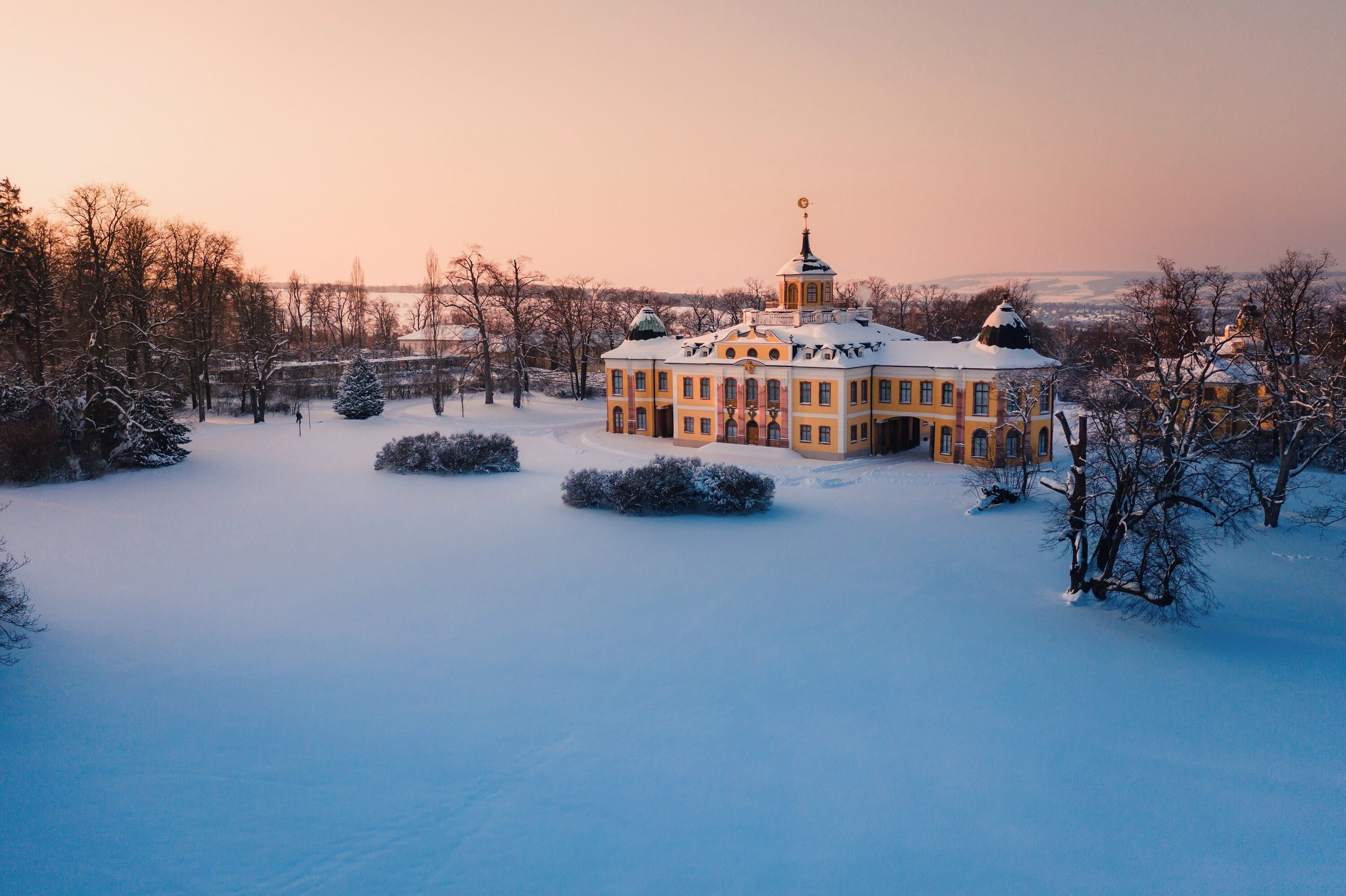 A large, historic building with a central tower, surrounded by snow-covered trees and a frozen landscape.