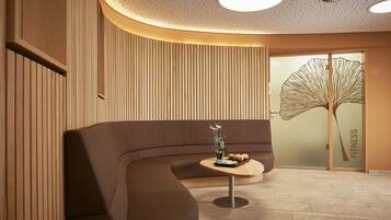 Ein modernes Interieur mit einem gebogenen Sofa, einem kleinen runden Tisch mit Pflanze und Obst, sowie einer Wand mit vertikalen Hol zleisten.