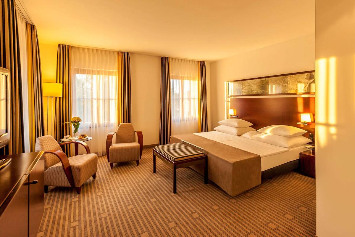 A hotel room with a bed, a desk, a chair, a small table, and a TV.