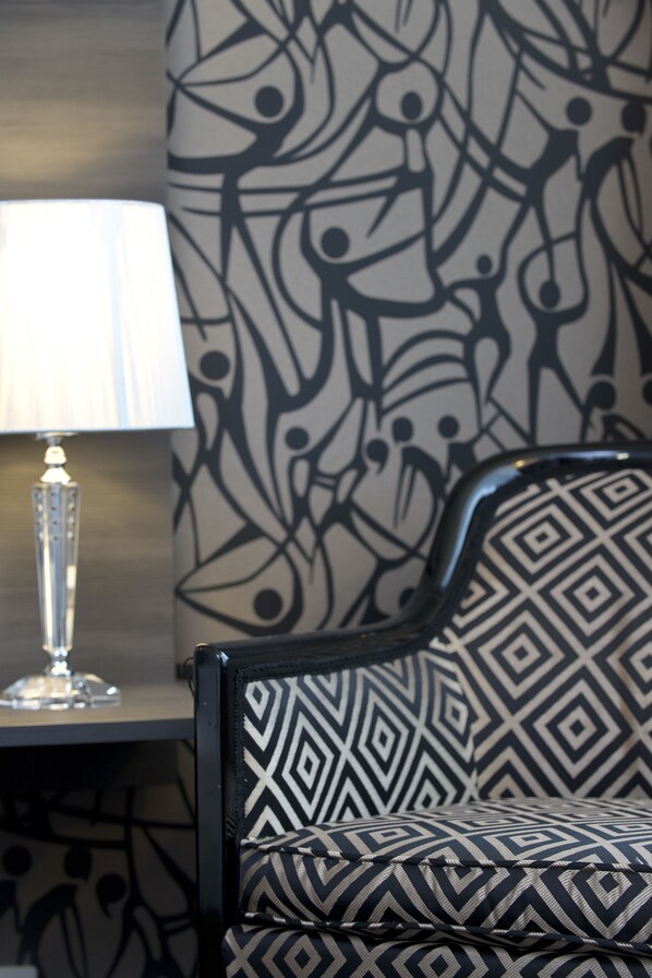 A room with a patterned wall, a lamp on a table, and a chair with a geometric design. - Park Hotel am Berliner Tor (Hamburg)