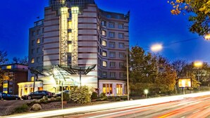Un hôtel à plusieurs étages au design moderne, caractérisé par une façade en verre imposante et une terrasse sur le toit.