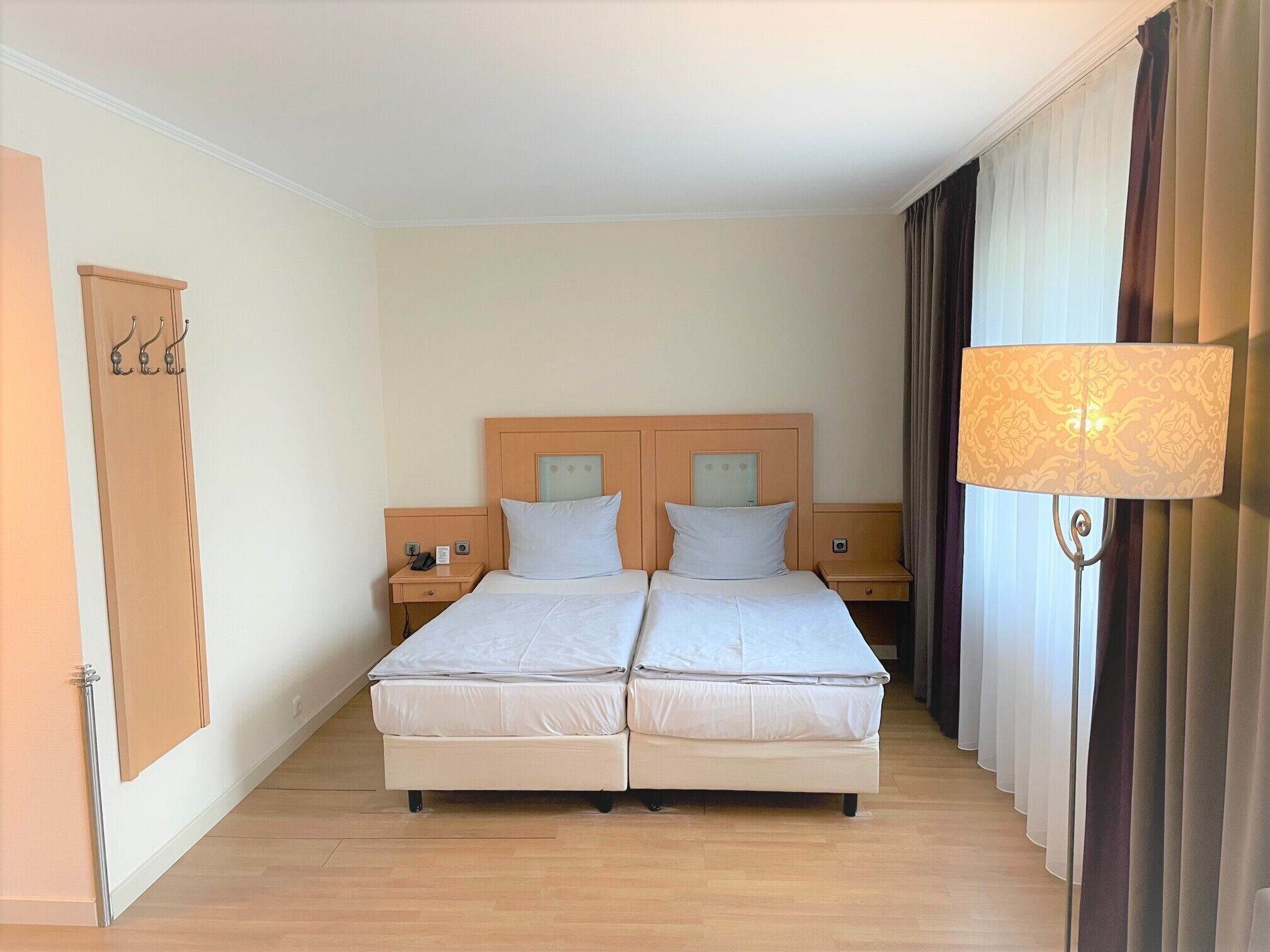 A double bed with a wooden headboard, two bedside tables with lamps, a wardrobe, and a large window with curtains.