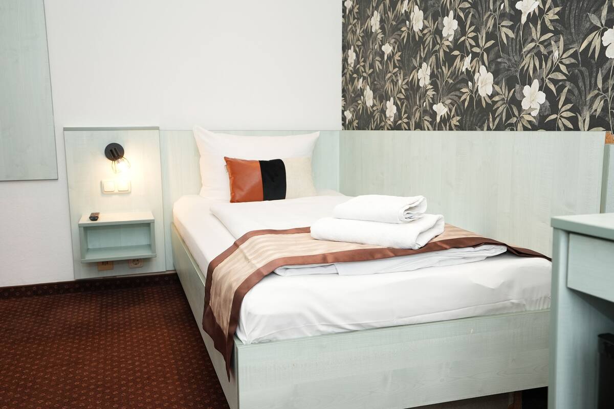 A neatly made bed with a striped blanket, a bedside lamp, and a floral wallpaper.