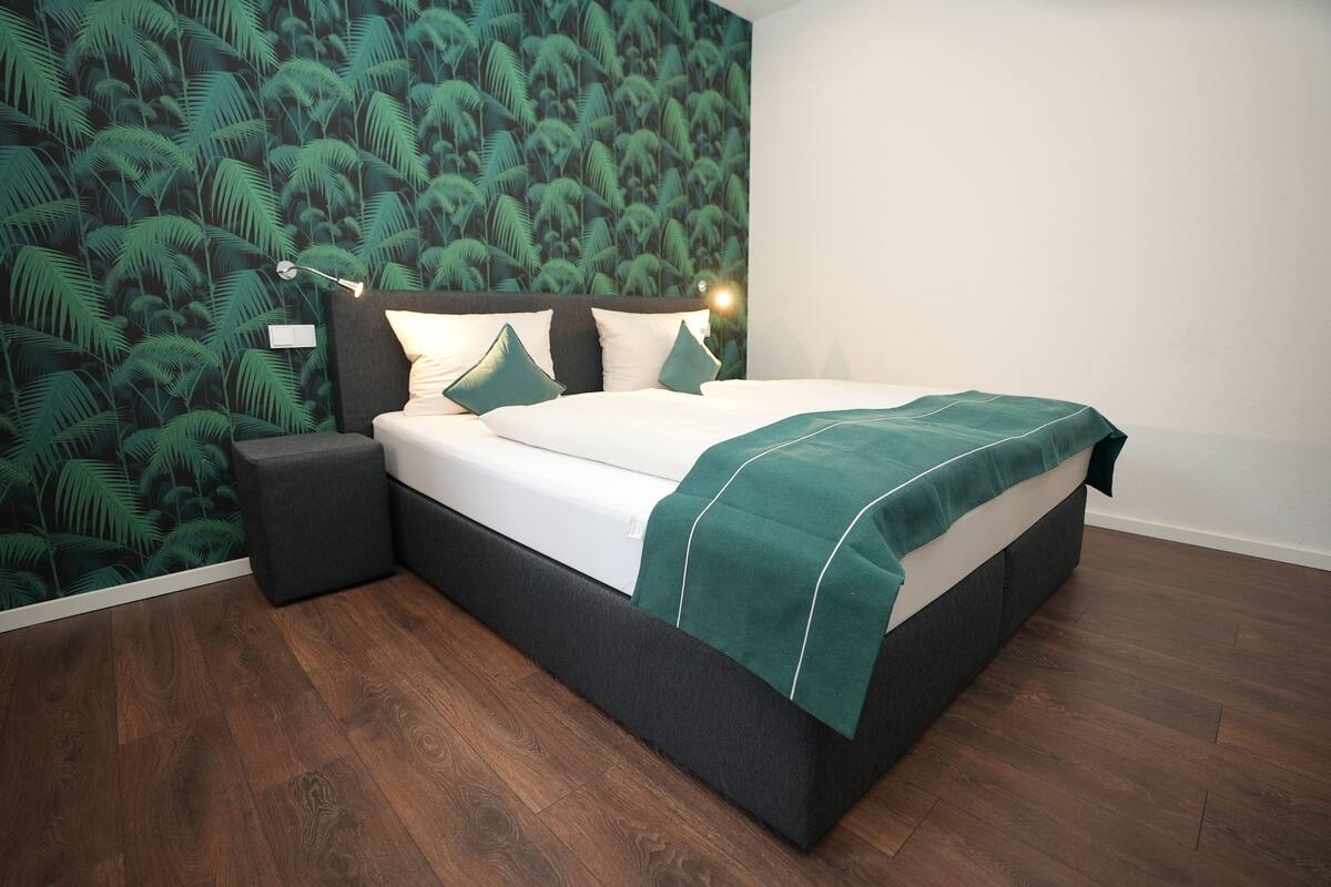 A modern bedroom with a bed, nightstands, and a wall with a tropical leaf pattern.