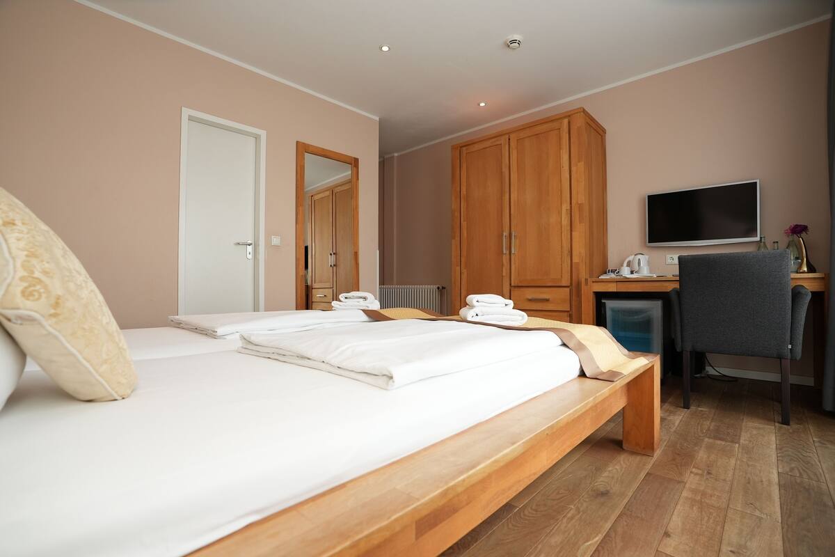 A bedroom with a bed, wooden wardrobe, desk, chair, and a television.