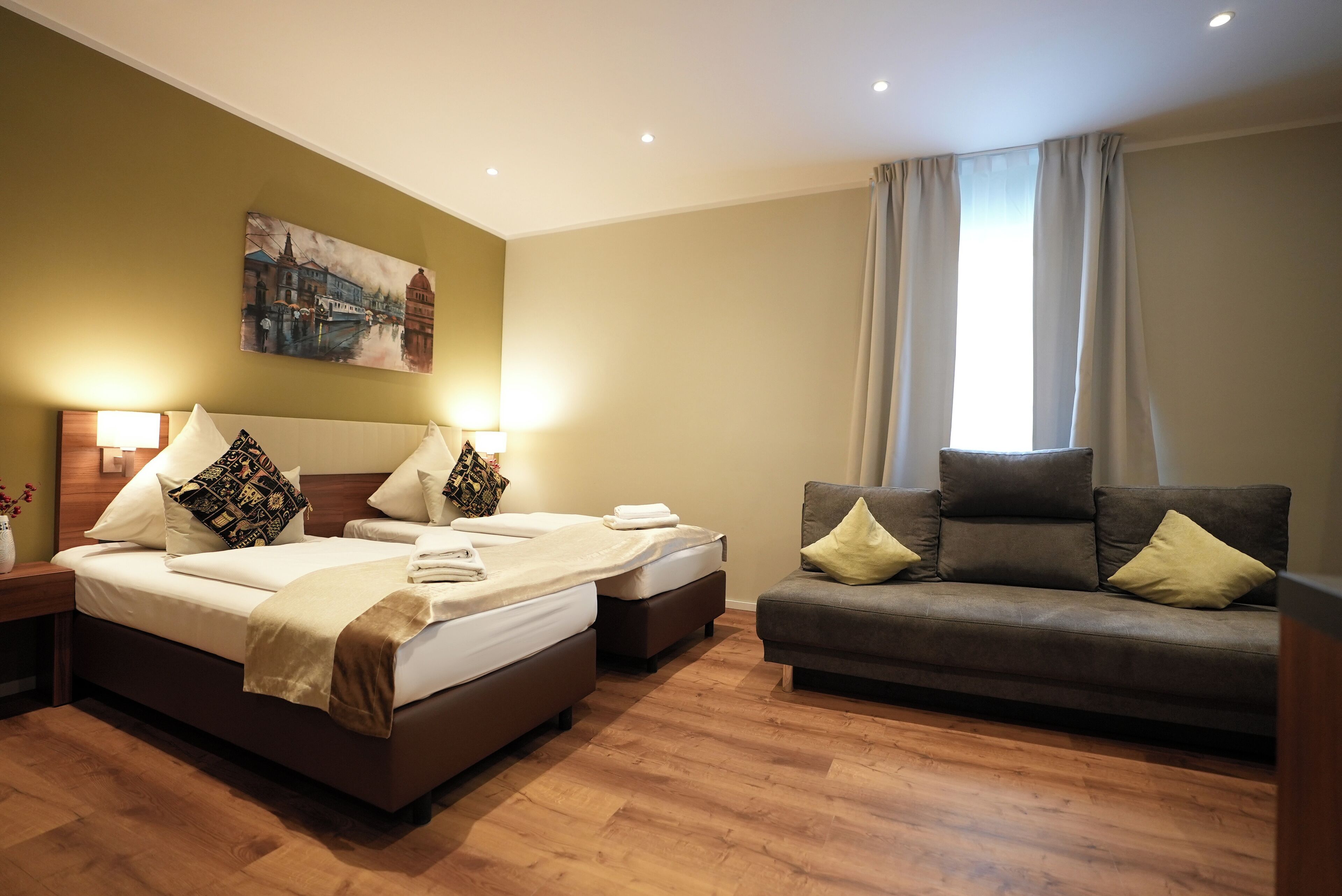 Une chambre d’hôtel avec un lit, un canapé, un tableau au mur et une fenêtre avec des rideaux.