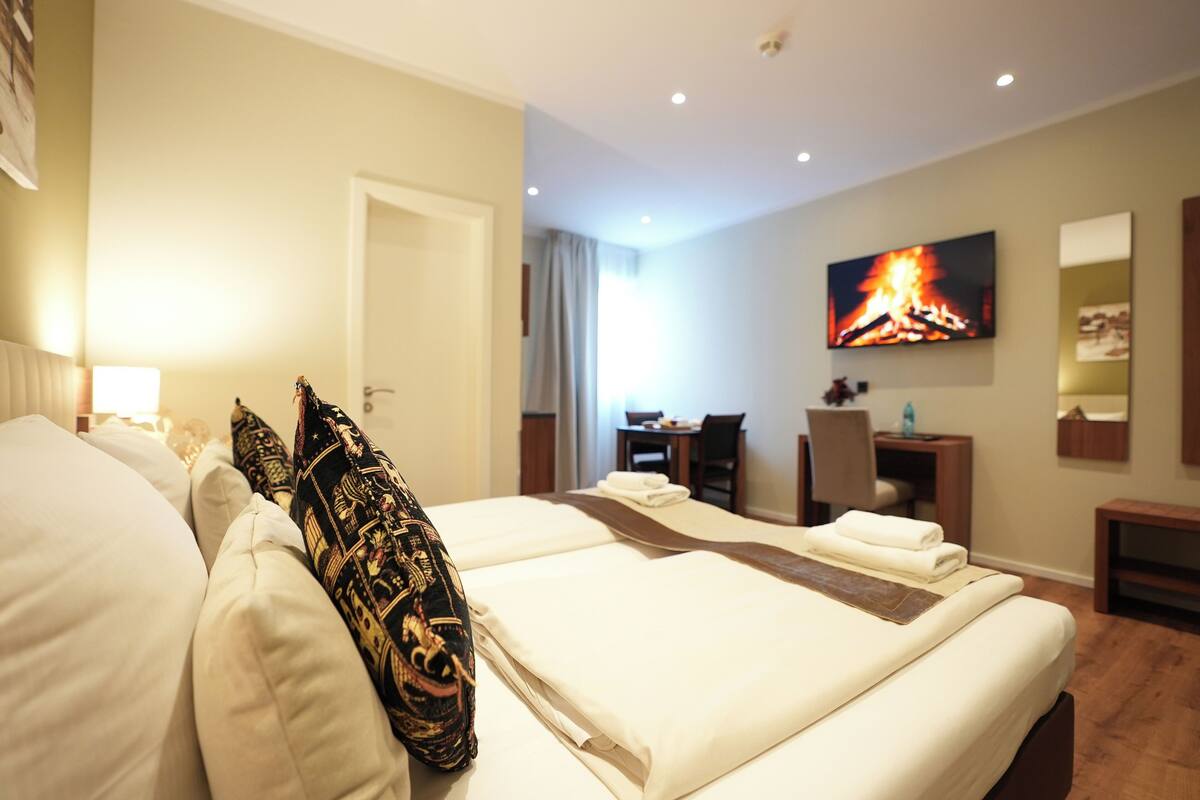 A hotel room with a bed, a desk, a chair, and a TV displaying a fire.