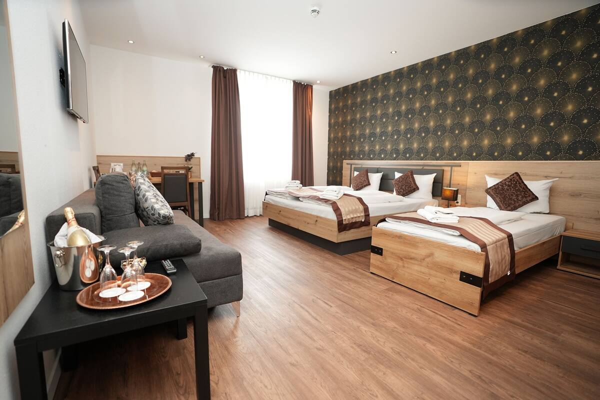 A hotel room with two beds, a sofa, a dining area, and a TV.