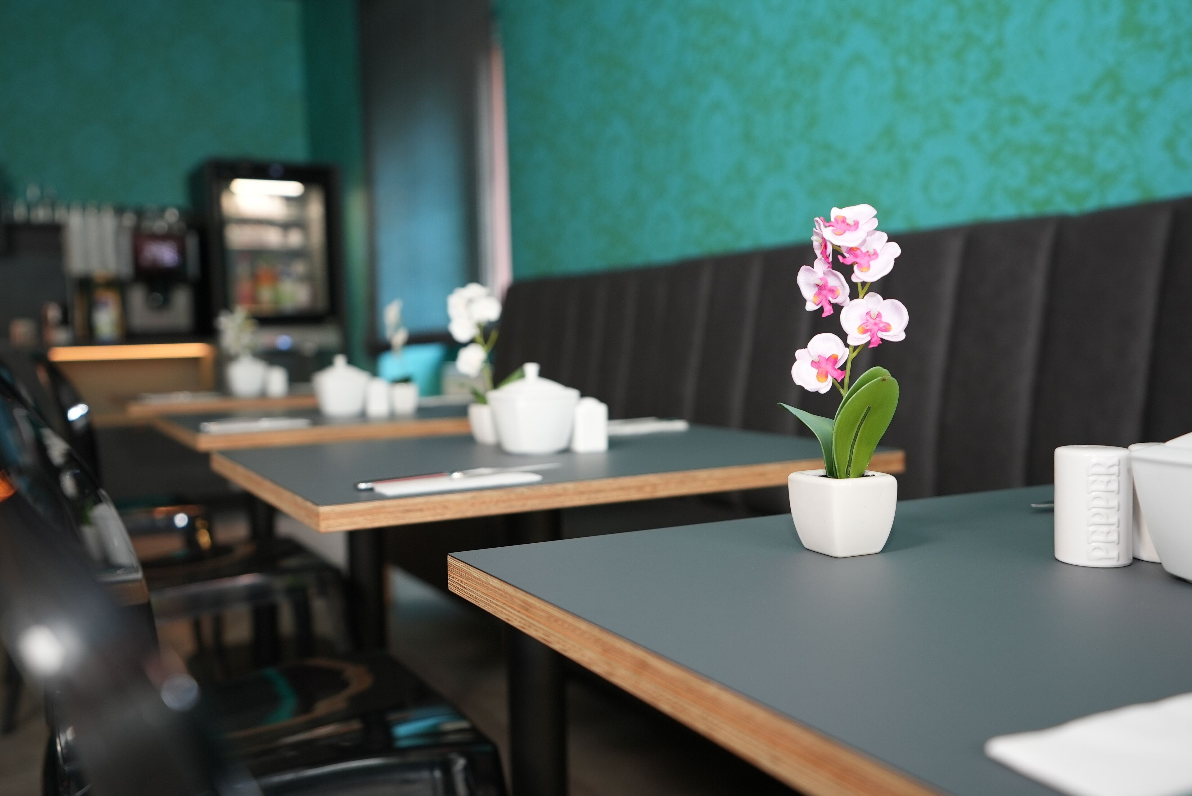 A restaurant with wooden tables, white teapots, and a potted orchid.