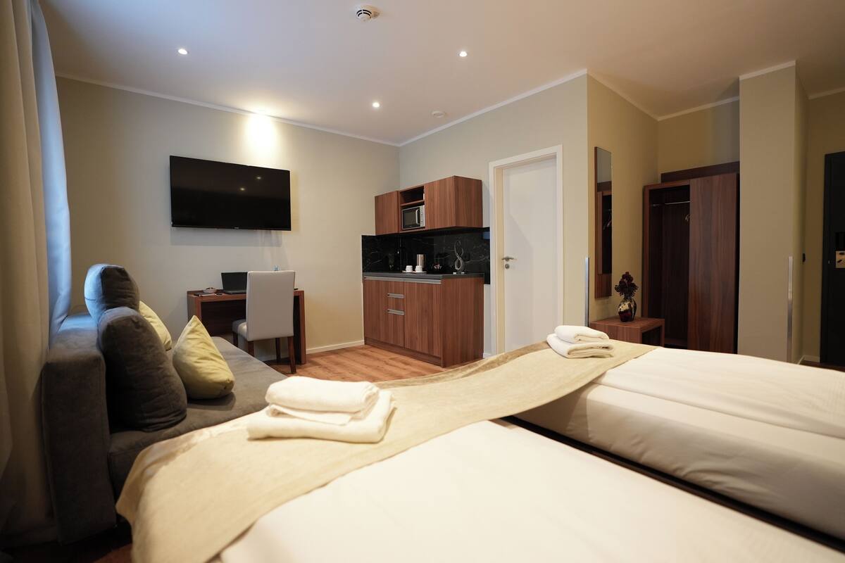 A hotel room with two beds, a flat-screen TV, a small kitchenette, and a desk.