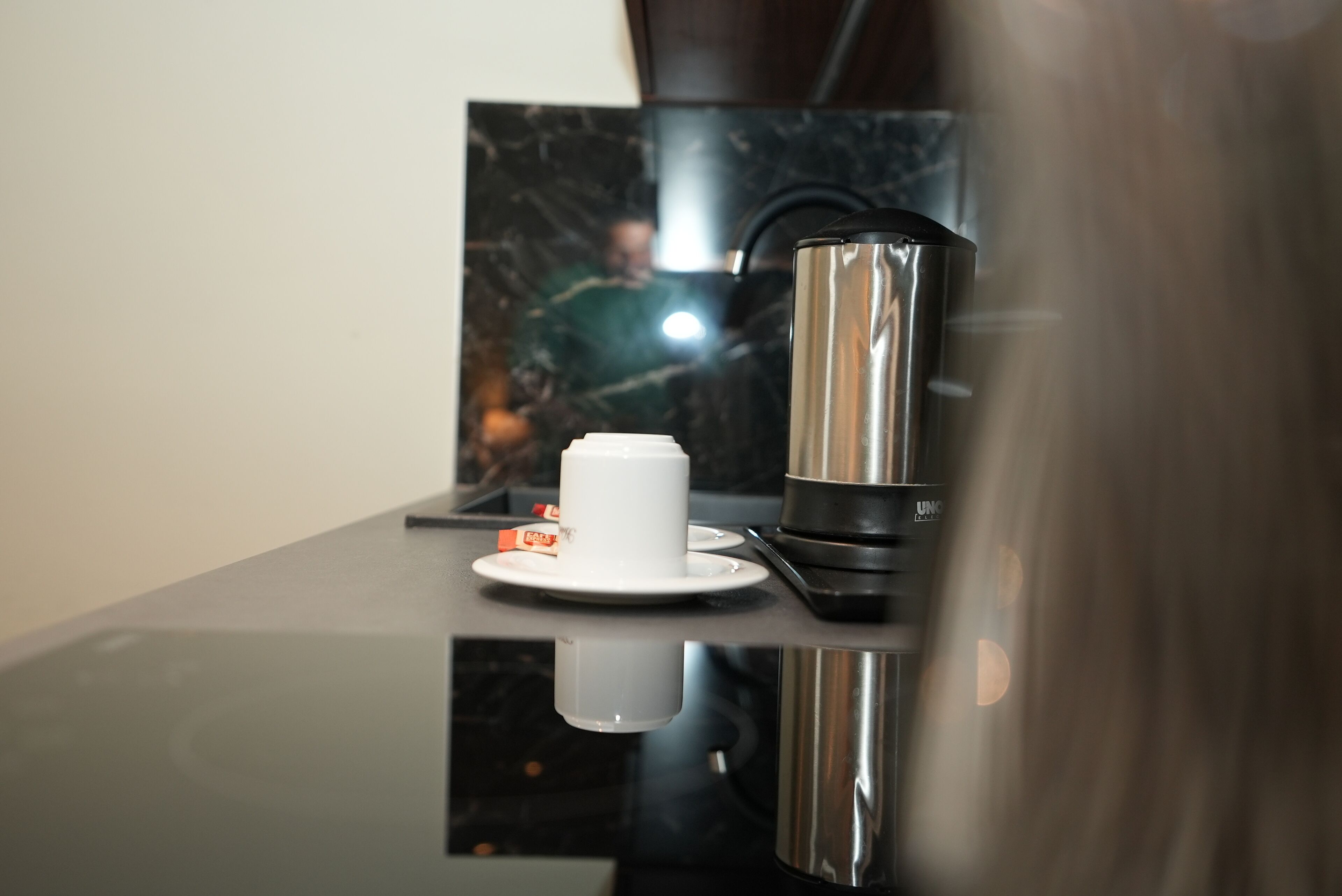 A modern kitchen with a coffee maker, a white cup, and a plate on a reflective countertop.