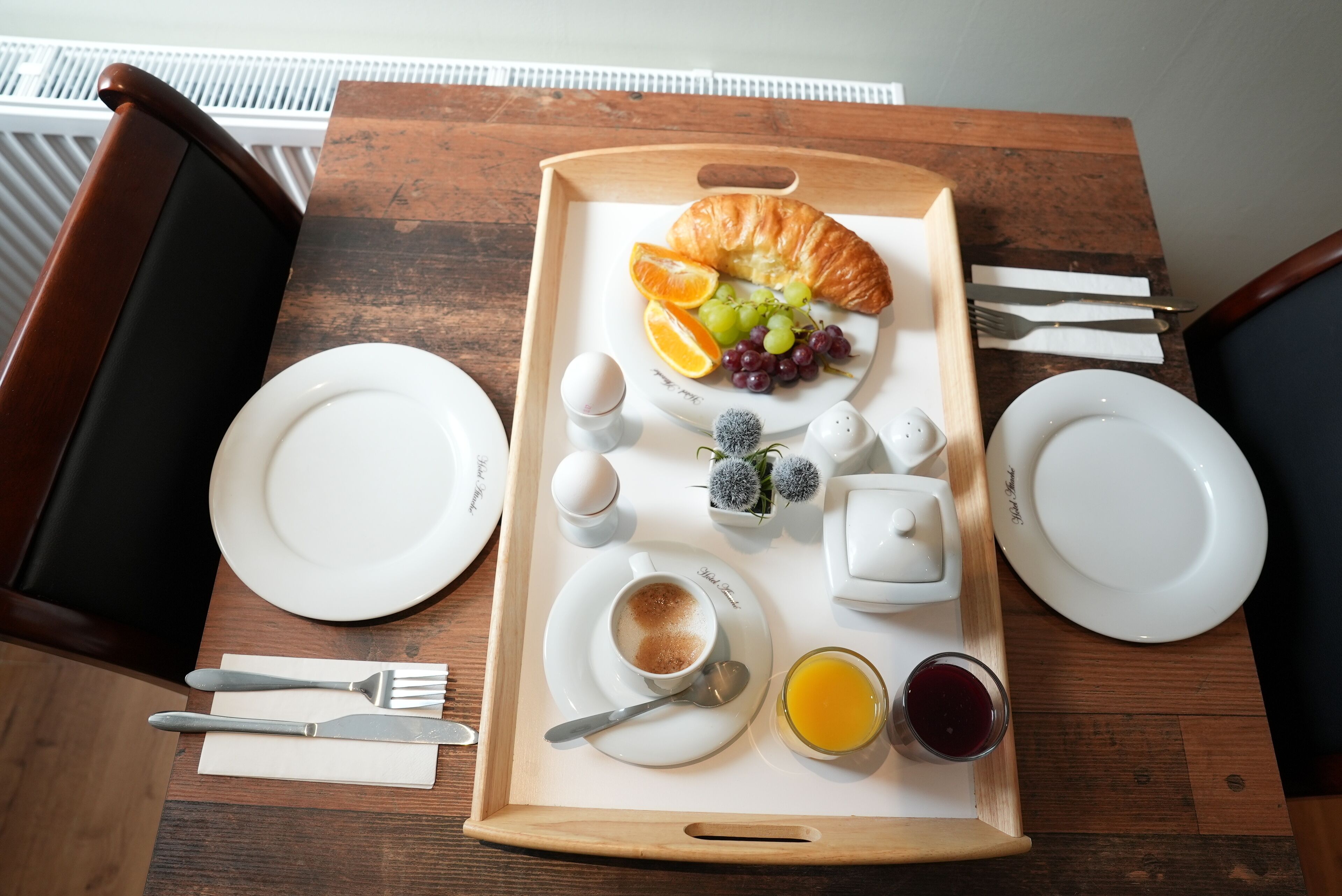 A breakfast tray with croissant, grapes, orange slices, coffee, and juice on a wooden table.