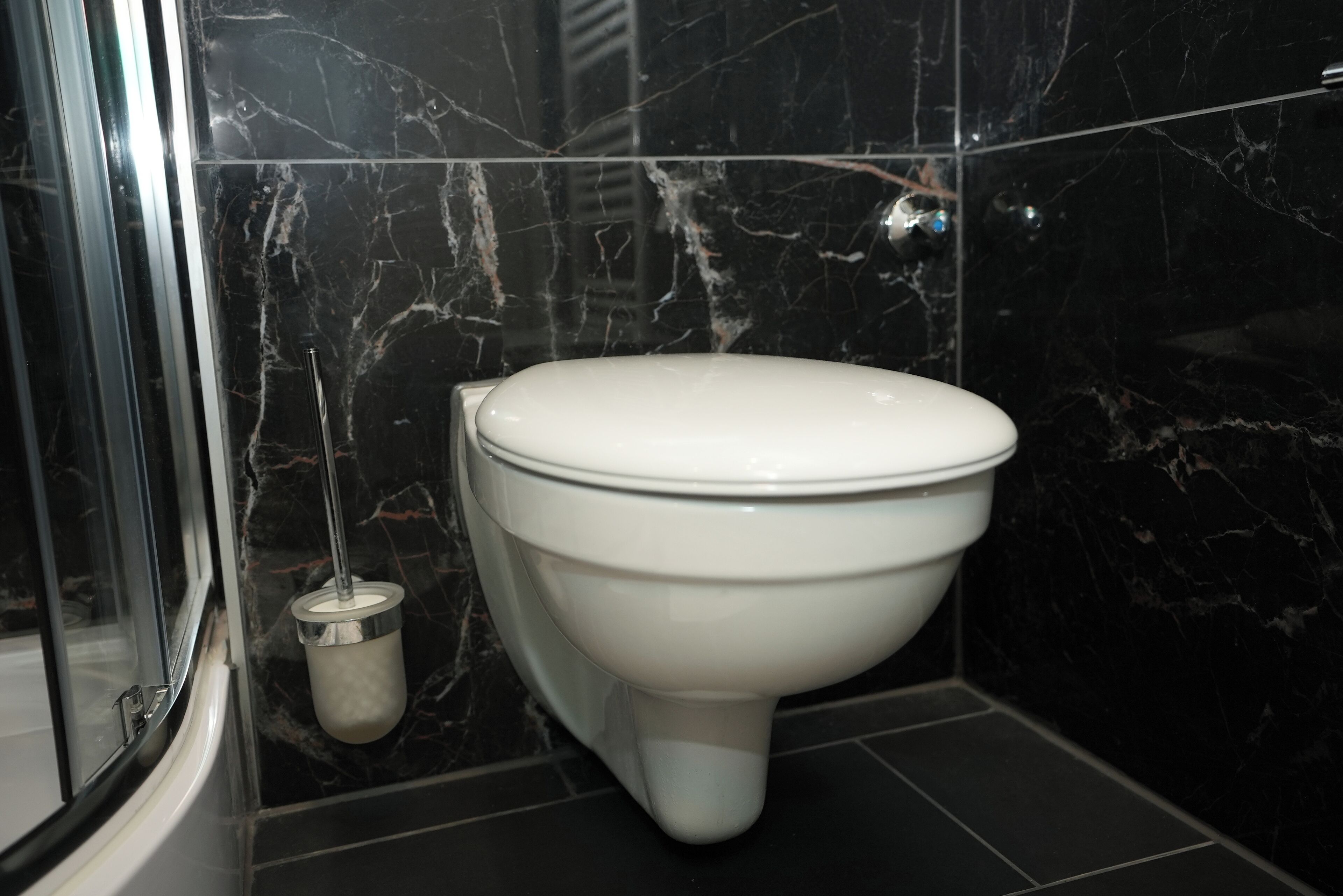 A bathroom with a toilet, a hand dryer, and a marble-tiled wall.