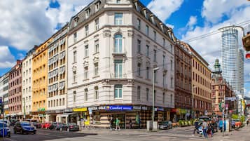 Ein historisches Gebäude mit Hauseingang an einer Ecke, einem sichtbaren Erdgeschoss mit Geschäften und einer gut sichtbaren Hotelschild.