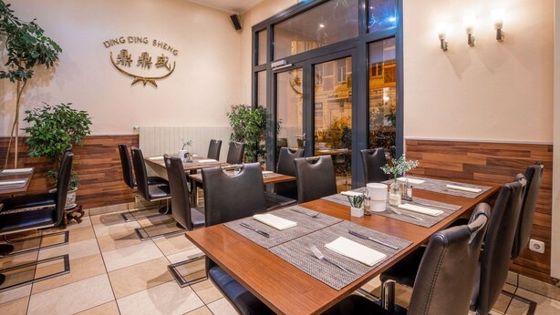 Un restaurante con mesas de madera y sillas negras, un letrero en la pared y un ventanal grande.