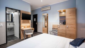 Una habitación de hotel moderna con una cama, un escritorio, una silla, un armario y un baño visible a través de una puerta abierta.