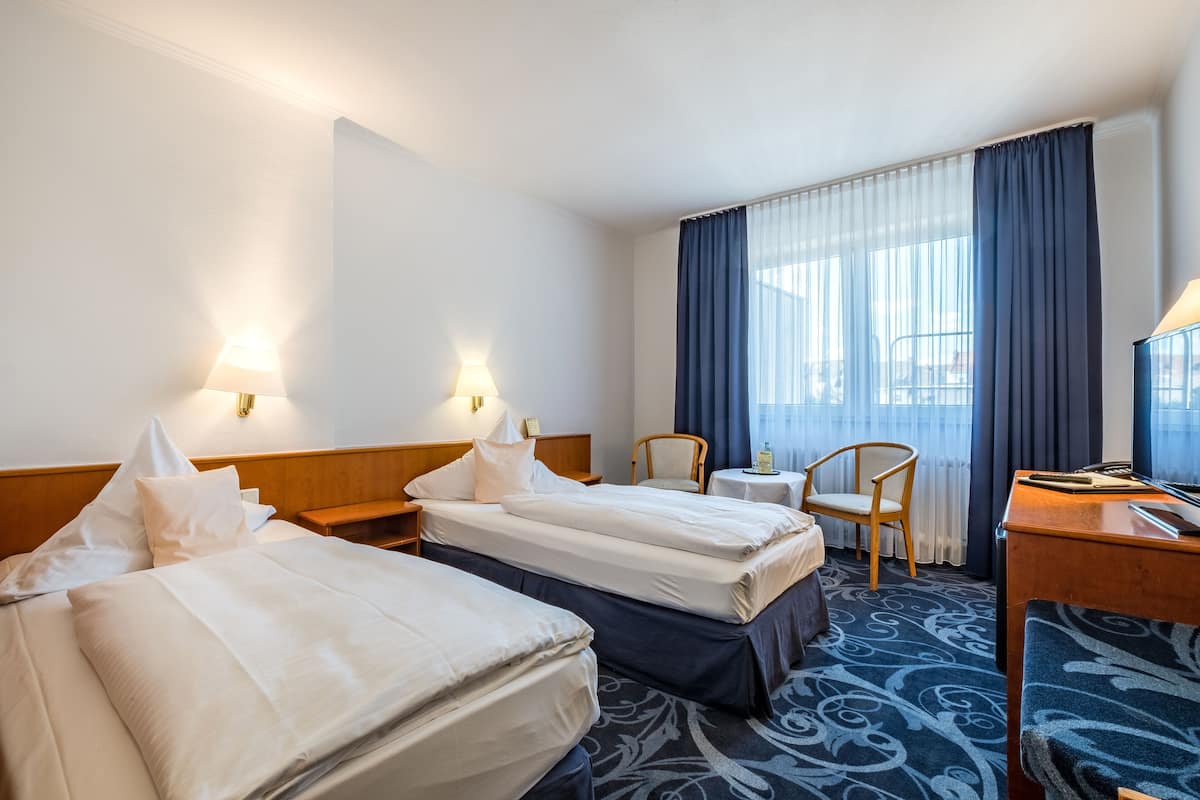 A hotel room with two beds, a desk, a chair, and a small table.