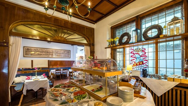 A buffet setup with various food items, a seating area with blue cushioned benches, and a decorative window with a floral pattern. - Hotel Gertrudenhof (Cologne)