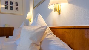 A neatly made bed with white linens and pillows, a wooden headboard, and wall-mounted lamps. - Hotel Gertrudenhof (Cologne)