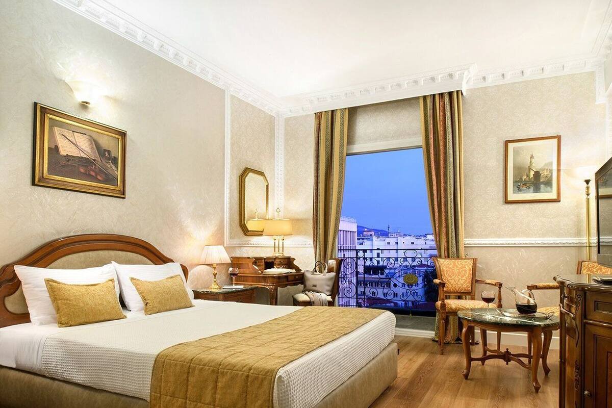 Quarto de hotel com uma cama grande, uma escrivaninha, uma cadeira, um espelho e vista para a paisagem urbana.