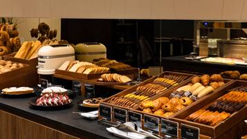 A breakfast buffet with various pastries, bread, and desserts.
