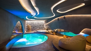 Un spa moderno con una amplia piscina climatizada, una silla de masajes y una pared de piedra.