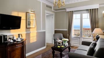 A hotel room with a television, a dining table with a bouquet of flowers, a sofa, a chair, and a view of the city through the window.