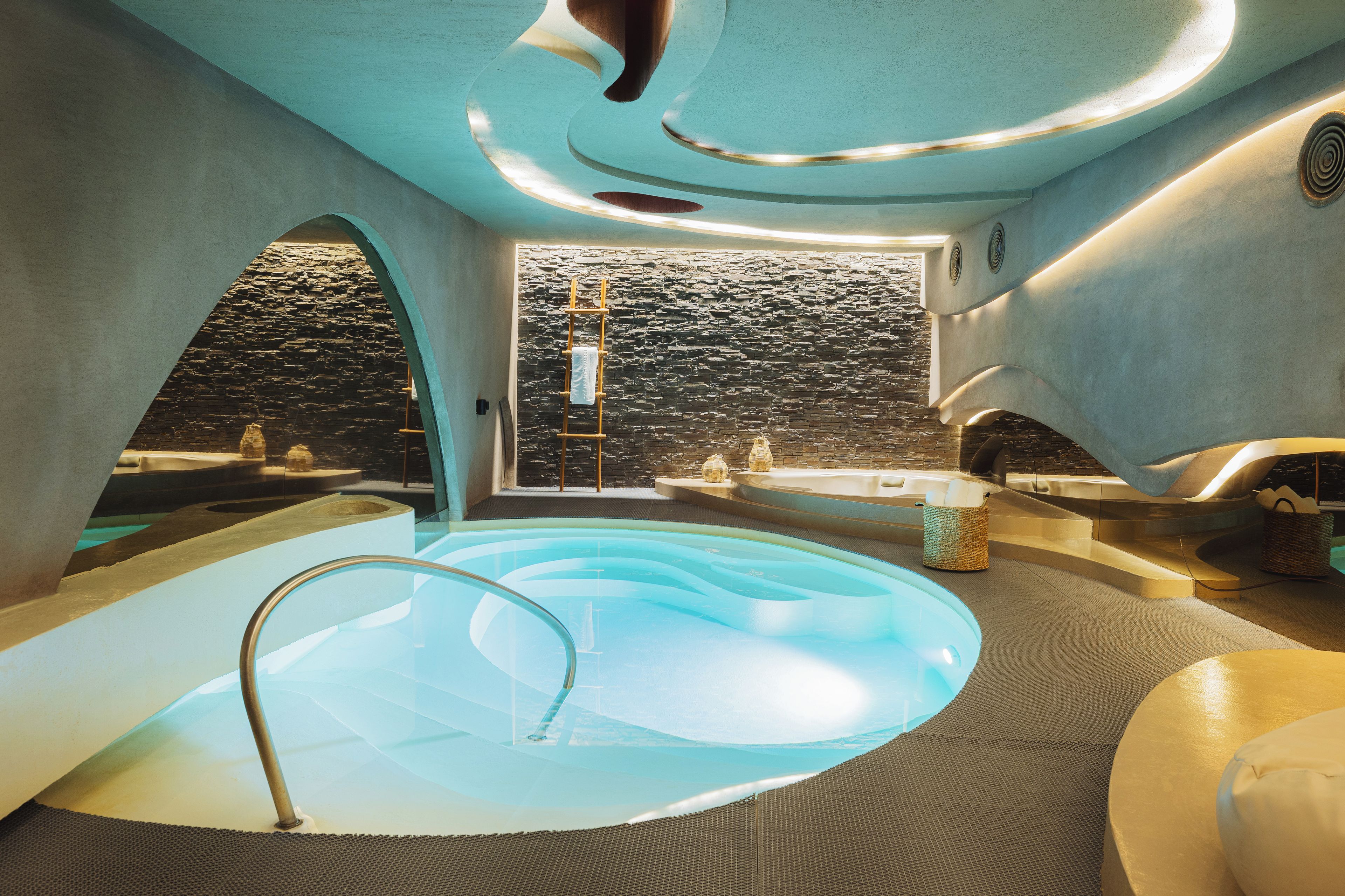 Un spa moderno con un jacuzzi central, paredes de piedra y vistas a un paisaje rocoso.
