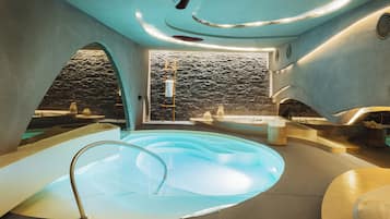 Un spa moderno con un jacuzzi central, paredes de piedra y vistas a un paisaje rocoso.