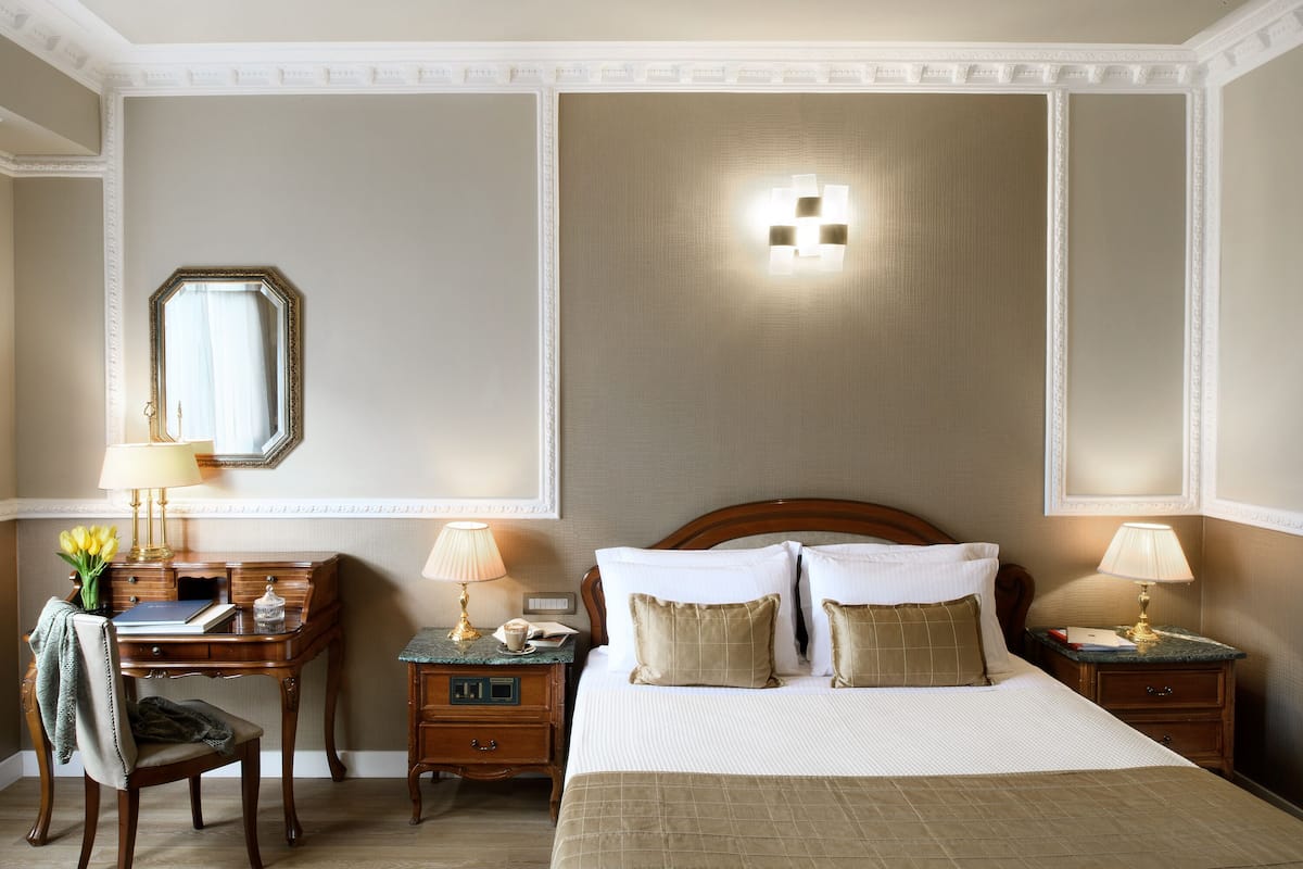 Quarto de hotel com uma cama grande, duas mesas de cabeceira, uma escrivaninha, uma cadeira e um espelho.