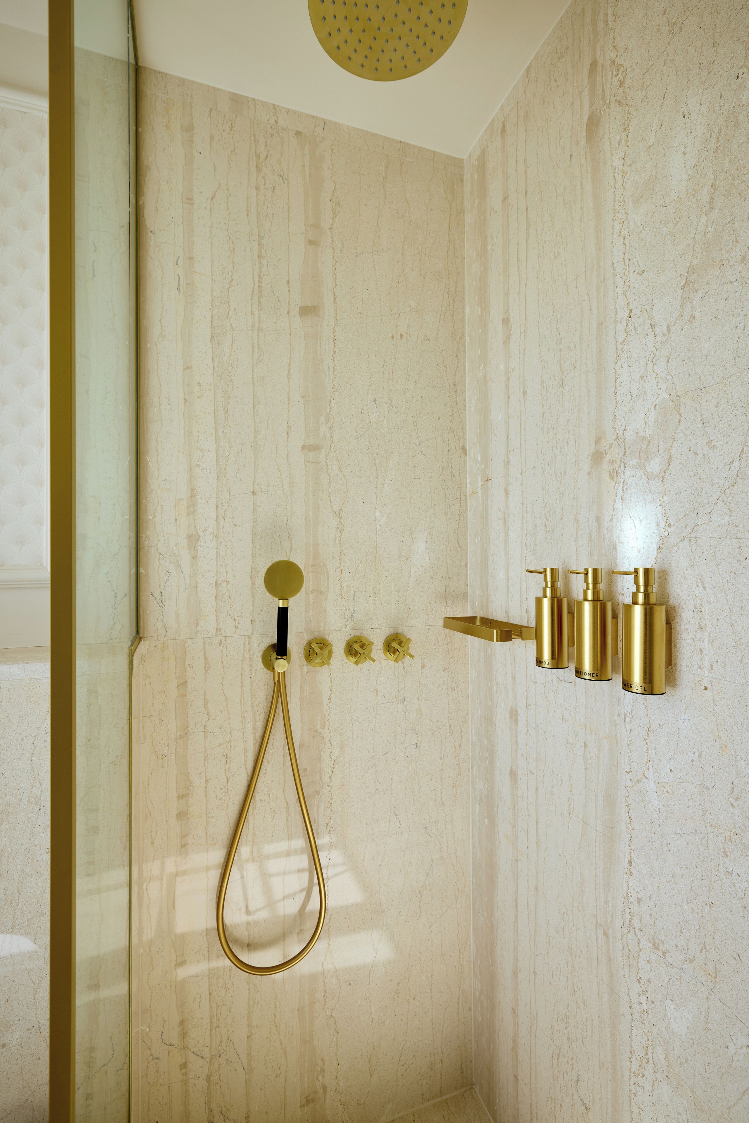 A bathroom with a marble wall, a gold showerhead, and gold fixtures.