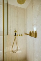 A bathroom with a marble wall, a gold showerhead, and gold fixtures.