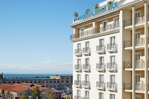 A hotel with a name sign, multiple balconies, and a view of the sea.