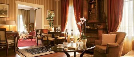 Habitación de hotel clásica con decoración tradicional, que incluye piso de madera, una mesa redonda con un jarrón de flores y un amplio armario de madera.