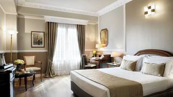 Quarto de hotel com uma cama grande, uma escrivaninha com abajur, uma cadeira e um quadro na parede.