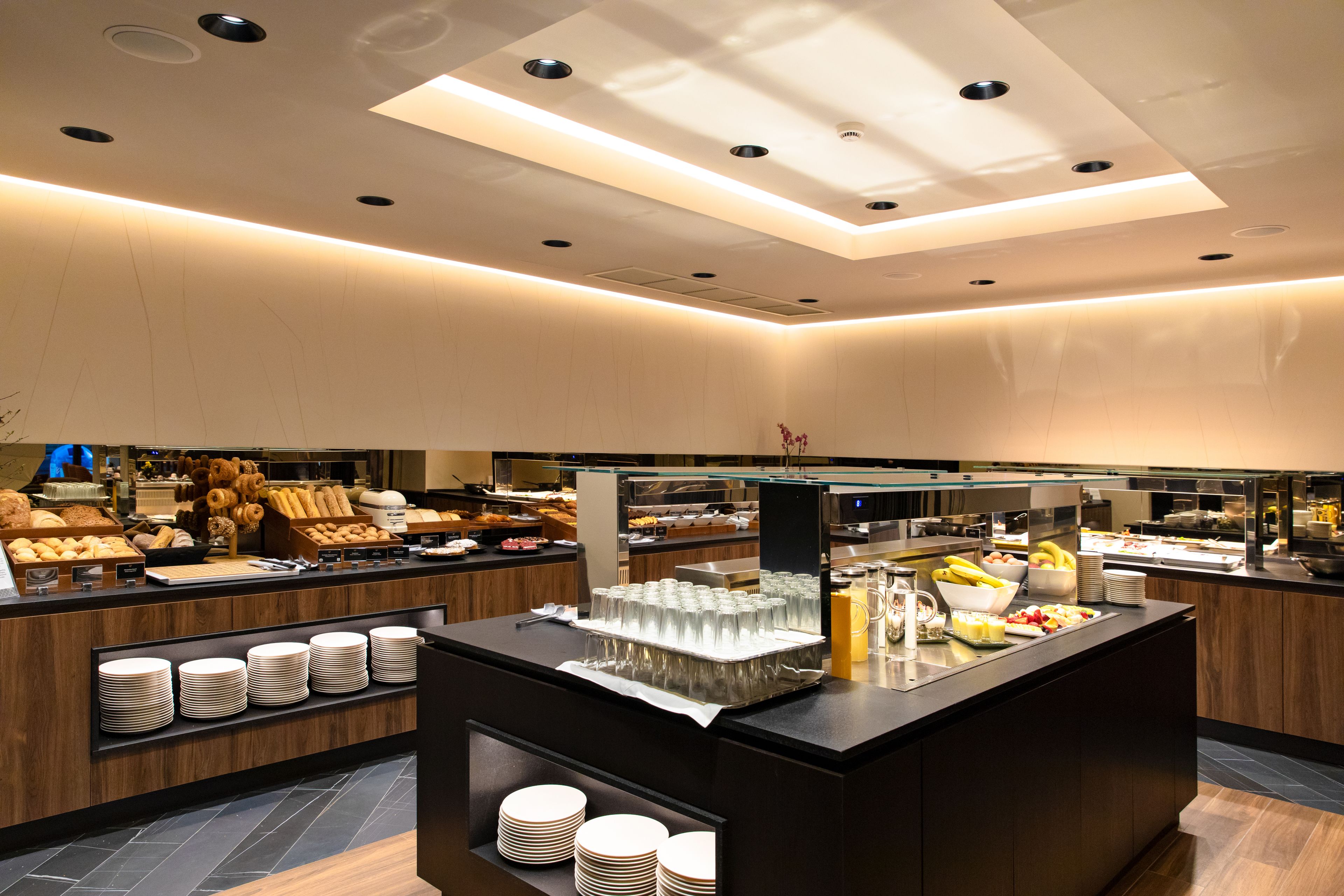 A modern breakfast buffet with a variety of food items, glassware, and stacked plates.