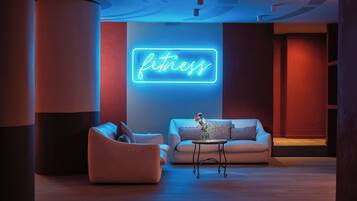 A modern lounge area with two sofas, a small table, and a neon sign reading "fitness".