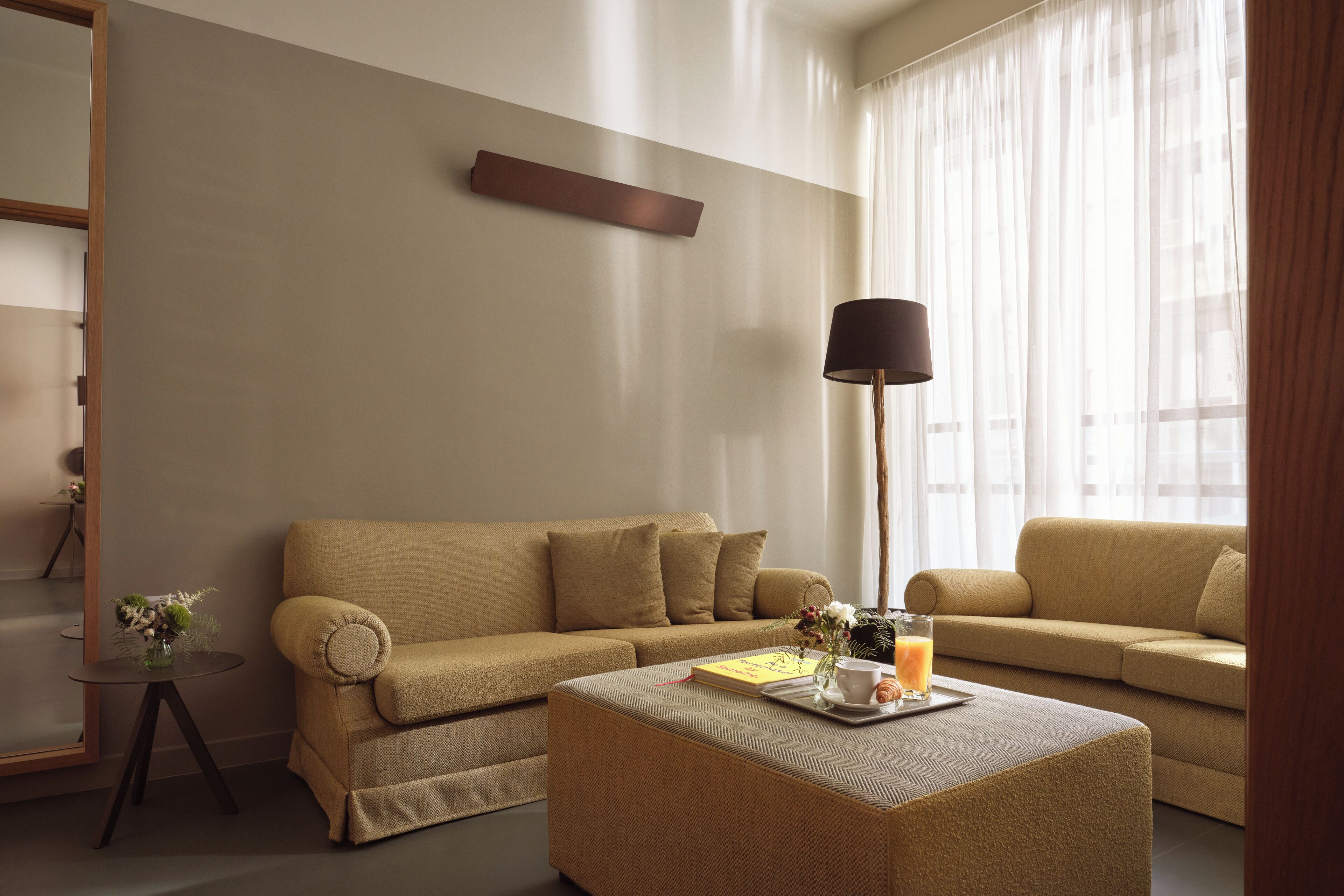 Un salon moderne avec un canapé beige, une table basse ronde sur laquelle se trouve un plateau avec divers objets, et un lampadaire.