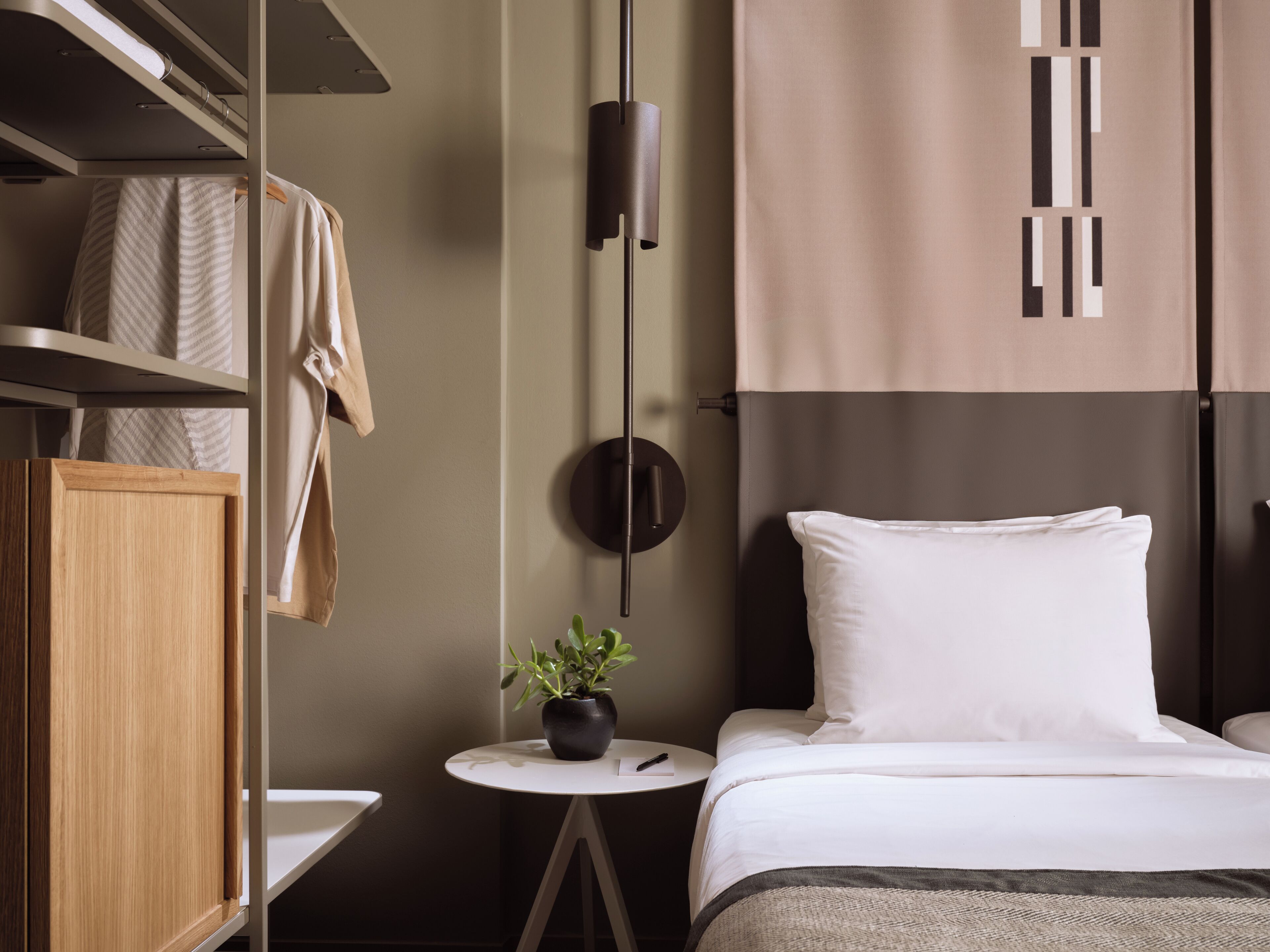 Une chambre à coucher moderne avec un lit, une petite table ronde ornée d’une plante, un luminaire suspendu et une armoire.