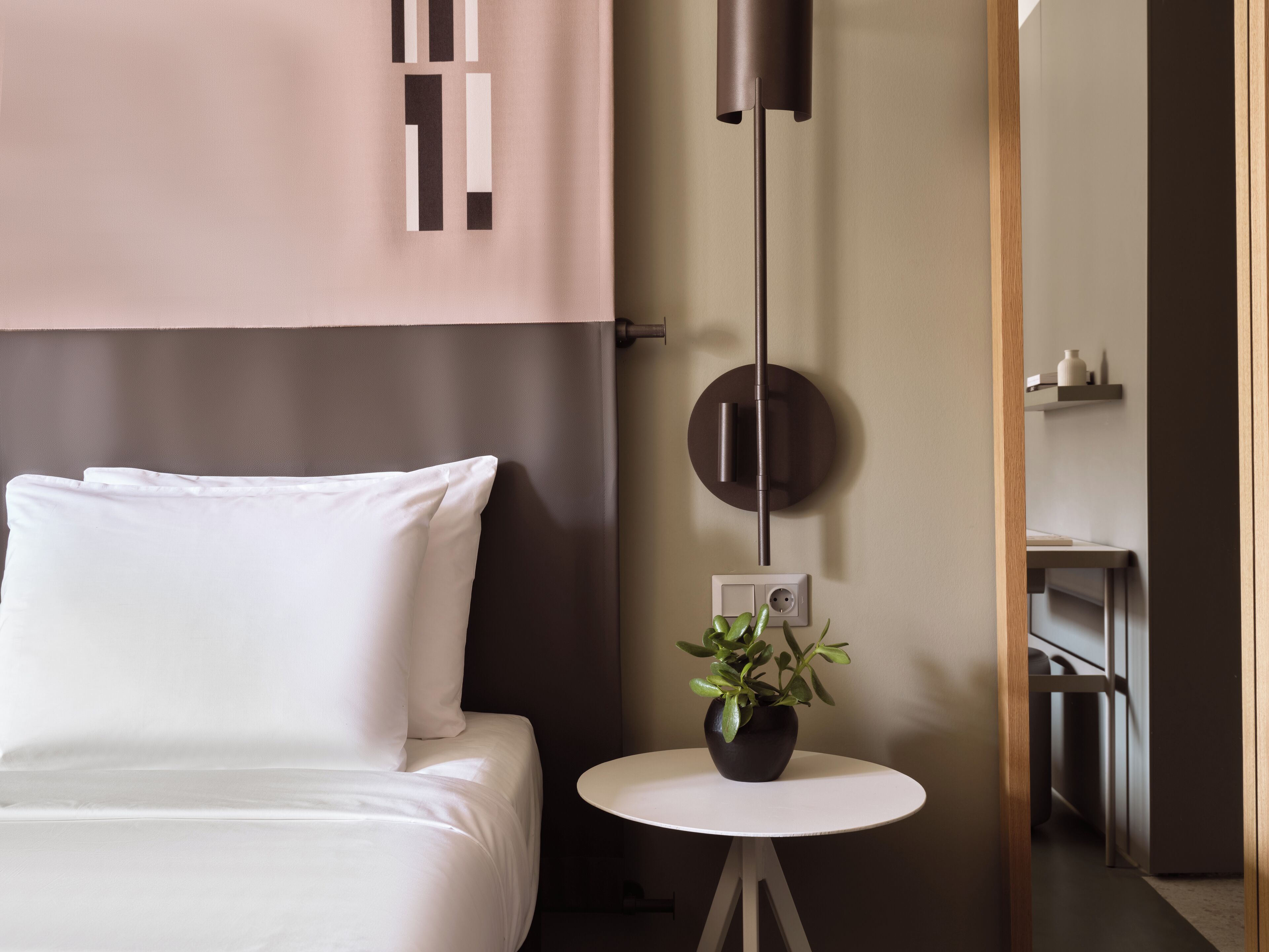 Una camera da letto moderna con un letto, una lampada a parete rotonda, un tavolino con una pianta e un comodino con presa di corrente.