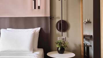 A modern bedroom with a bed, a round wall-mounted light, a small table with a plant, and a bedside table with a power outlet.