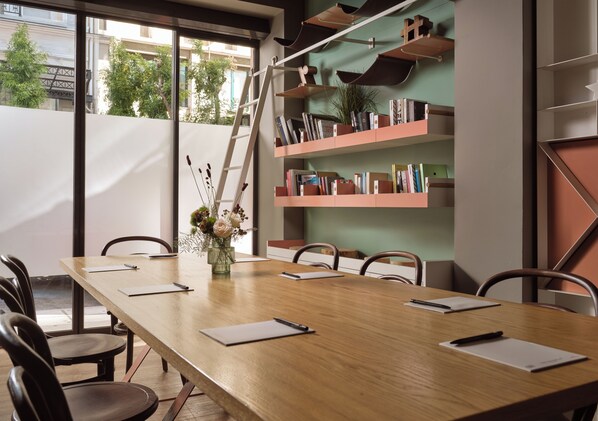 A conference room with a long wooden table, six chairs, a ladder, and bookshelves with books and plants.