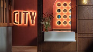 Un área de recepción con un cartel que dice 'CITY', un mostrador de recepción de madera y una lámpara con forma de llave.