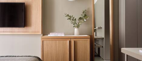 Ein modernes Hotelzimmer mit einem Holzkasten, einem Flachbildfernseher, einer weißen Vase mit grünen Blättern und einer runden Leuchte.