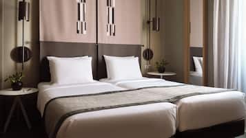 A modern hotel room with a large bed, two bedside tables, a small round table, and a potted plant.
